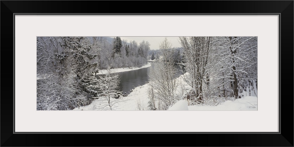 River and surrounding trees blanketed in snow from a recent snowfall, giving the landscape a quiet, dreary feel.