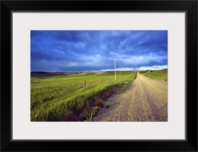 Landscape, oversized photograph of a gravel road, open fields on wither side, beneath a stormy sky of swirling clouds, in ...