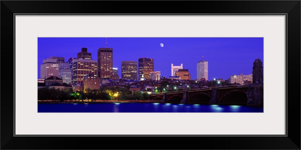 Panoramic canvas of a cityscape on the waterfront with a bridge leading to it and a bright moon in the evening sky.