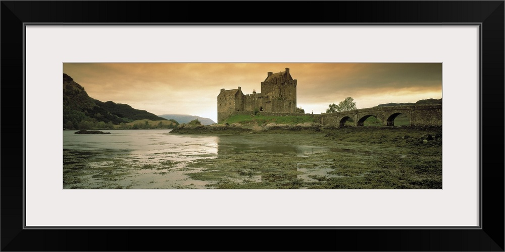 Wide angle photograph taken of a castle in Scotland under a dusk sky with wet land shown in the foreground and hills shown...