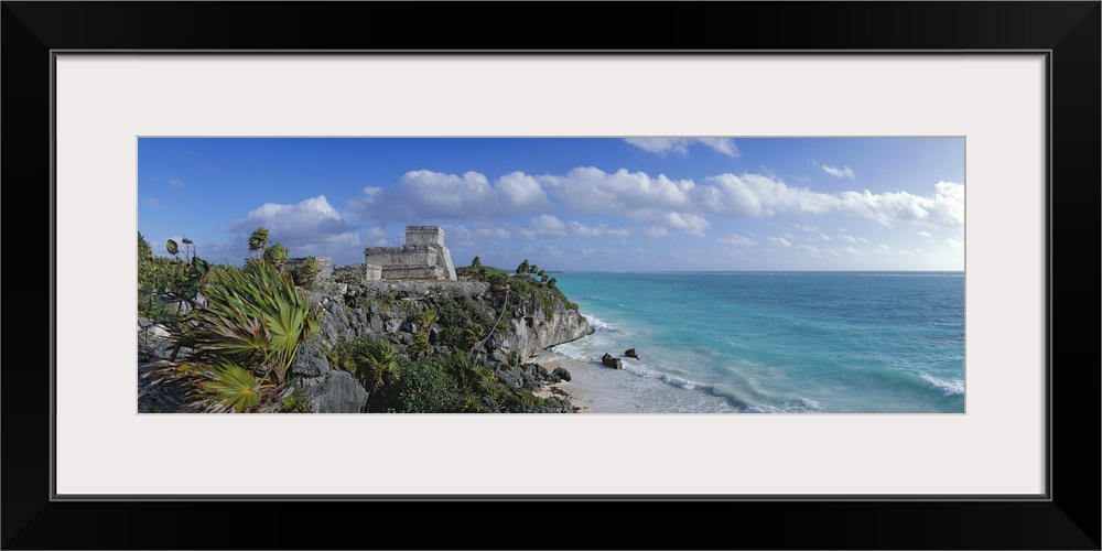 Large panoramic piece of ruins on a cliff off the coast of Mexico. Foliage and rocks are seen close up and also line the c...