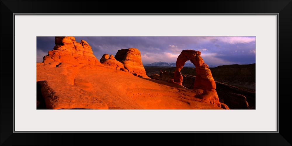 A landscape photograph that is a panoramic shot of a wind eroded rock face illuminated a sunset.