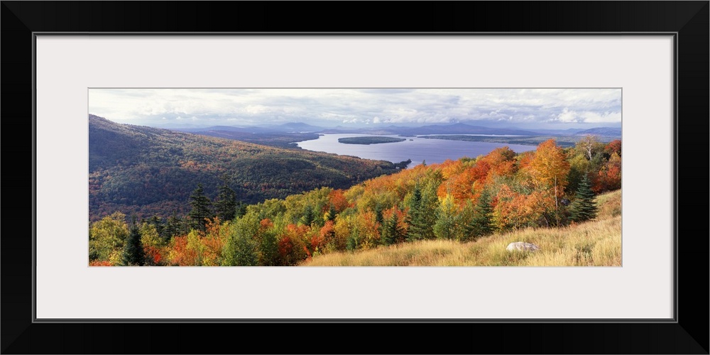 Wide angle photograph overlooking autumn colored trees on a hillside, dense forest surrounds Mooselookmeguntic Lake in the...