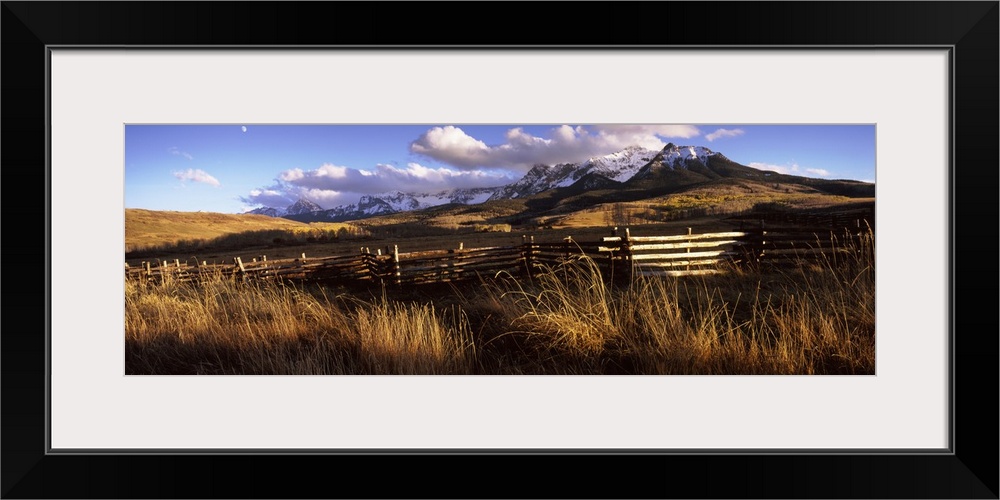 A large panoramic picture of Colorado mountains with a fence and tall grass in the foreground.