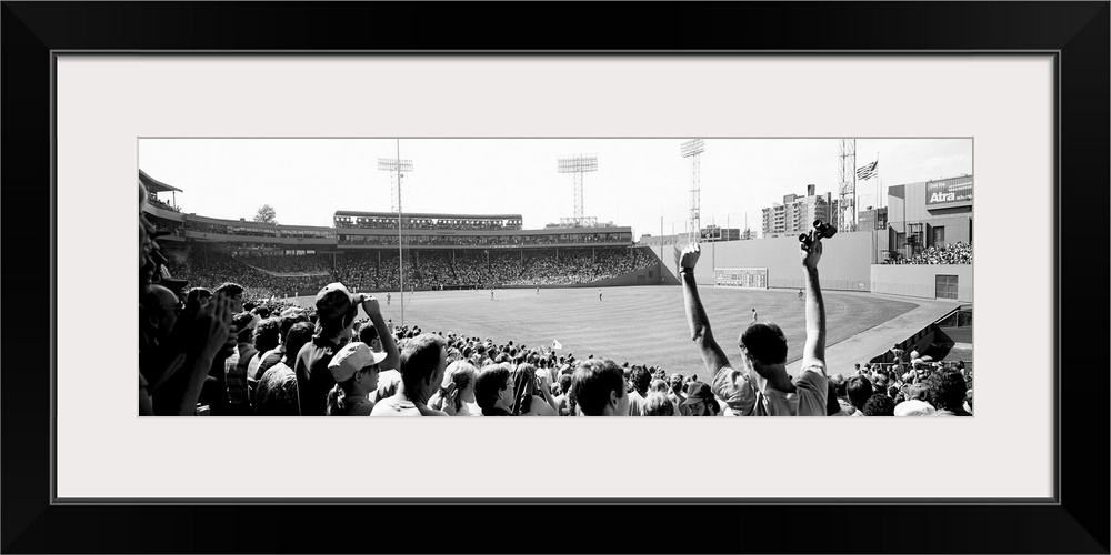 Big, panoramic black and white photograph of Fenway Park in Boston, with fans standing and cheering in the foreground.