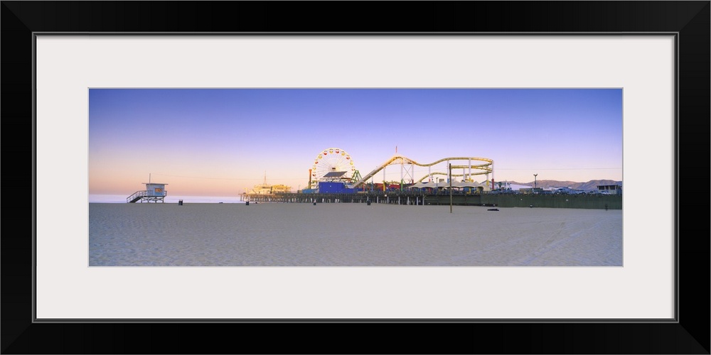 This is a panoramic photograph of a board walk carnival taken from a sandy beach at twilight.