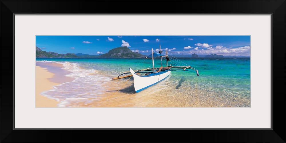 A panoramic photograph of a tropical beach with mountains and island in the background with a boat pulled up on shore from...