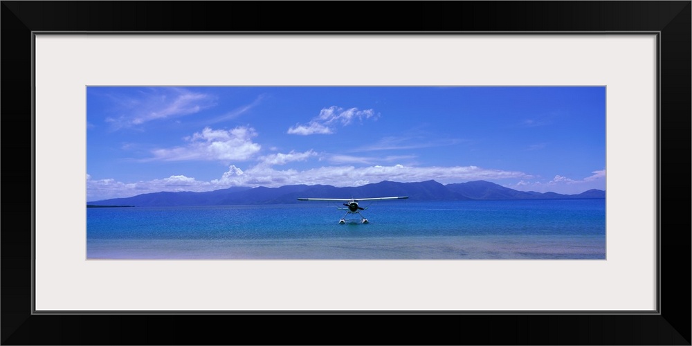 Private propeller plane floating on the water near the shoreline with low mountains and cloudy skies overhead.