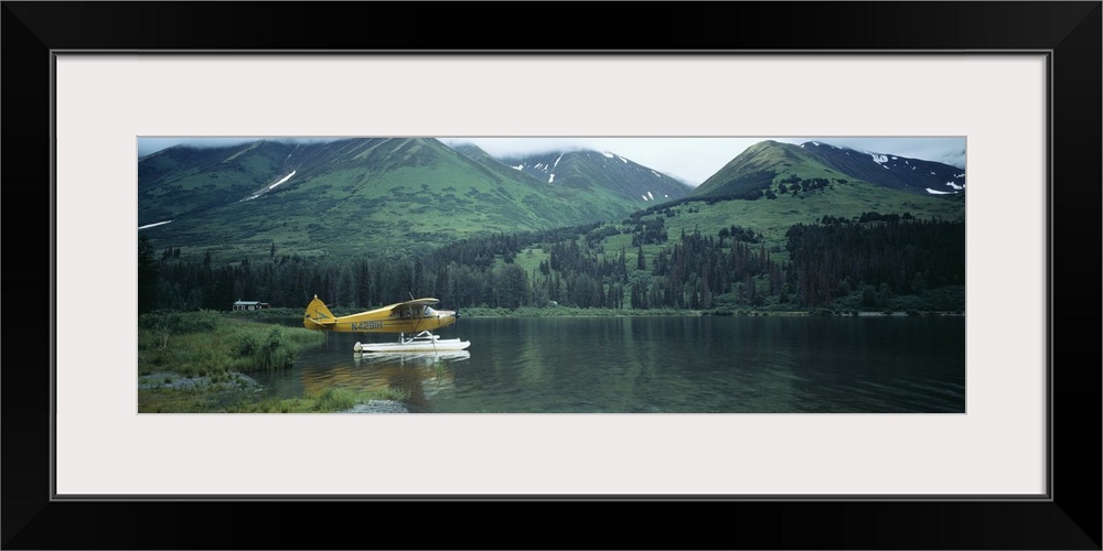 Panoramic photograph of airplane on skis in lake with mountains in the distance.