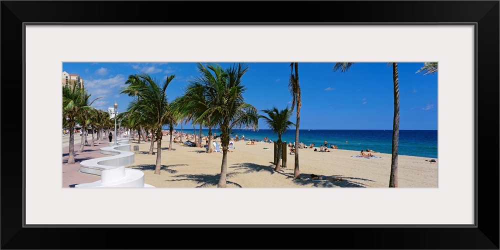Panoramic photograph showcases a lively beach scene scattered with people within Florida that has palm trees dusted throug...