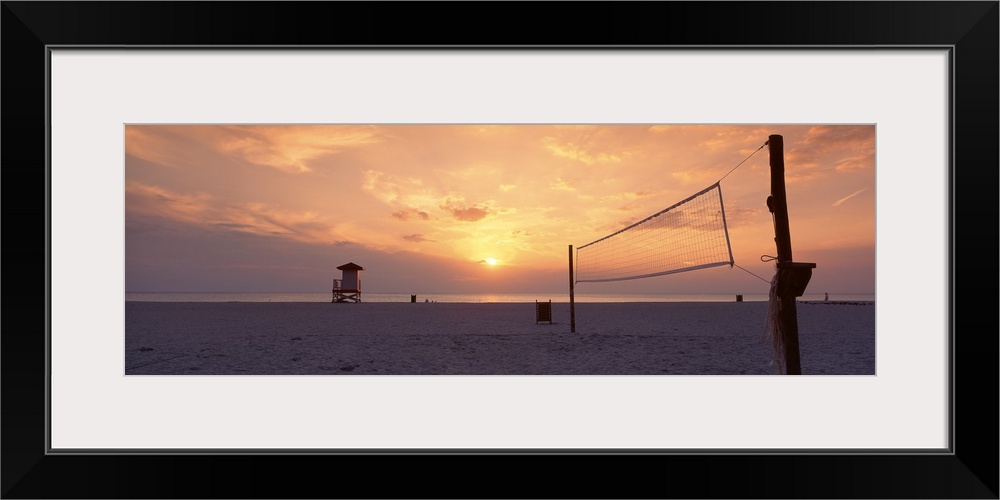 The sun sets over a sandy beach which is empty except for a lifeguard tower and a volleyball net.