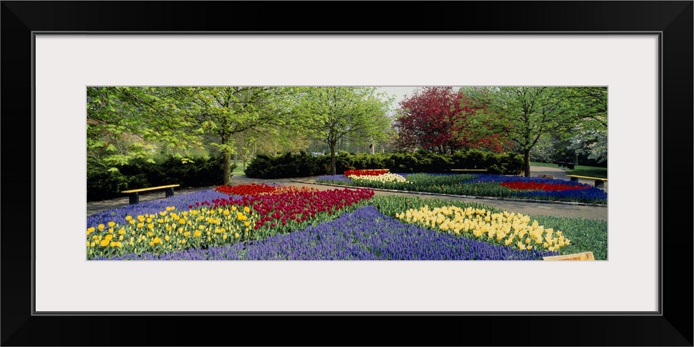 This panoramic picture was taken on a beautiful day of flower gardens inside a park.