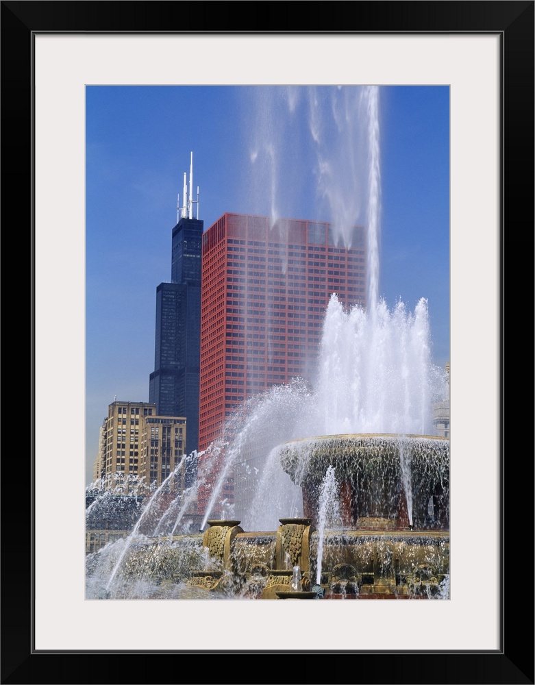 A large fountain shoots water up high with a view of skyscrapers in Chicago shown in the background.