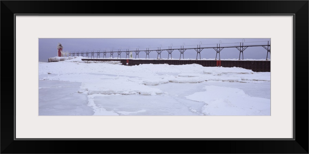 Panoramic photograph of pier stretching into ice covered river leading to a tower with a guiding light at the top.