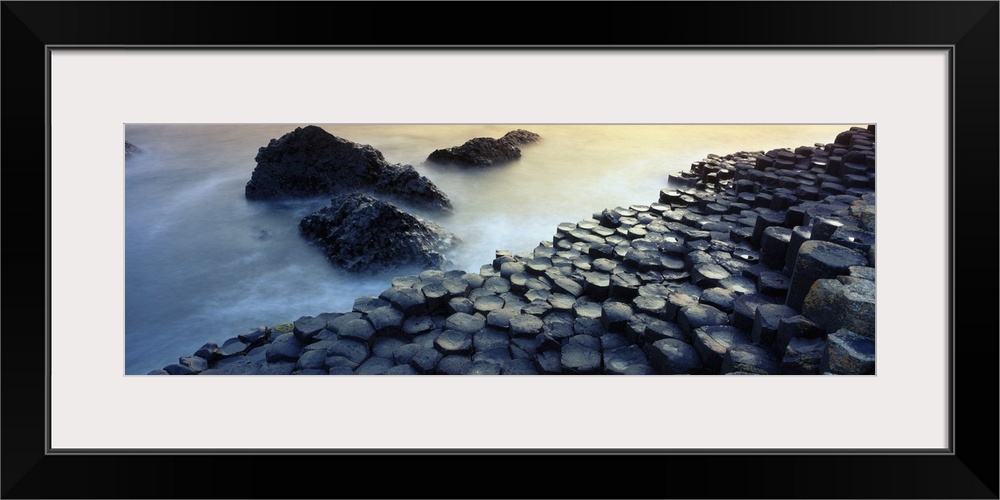 Panoramic photograph of rocky shoreline with large stone formations rising from mist covered ocean.