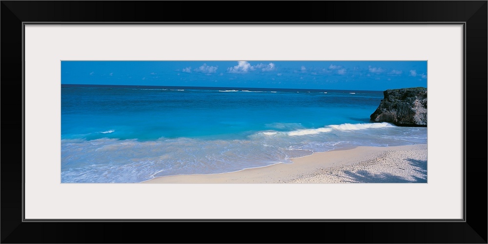 This is a panoramic photograph of small waves breaking on a sandy tropical beach.