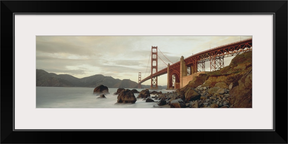 Panoramic photograph shows a body of water slowly crashing into the rocky shores that sit next to this landmark overpass l...