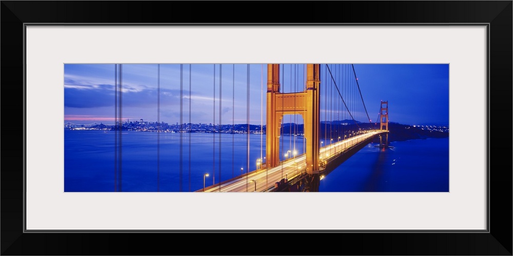 Long and narrow photo print of an up close view of the Golden Gate Bridge lit up at night with cars driving across it.