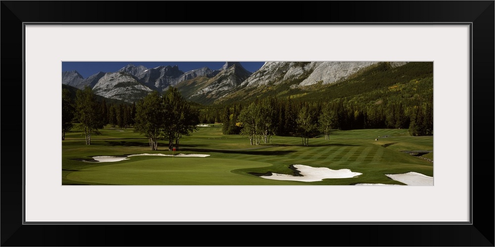 Panoramic photograph taken on a golf course of one of the holes that is surrounded by a mountain view.