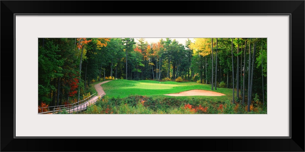 Panoramic photo of a golf green in the Northern United States. A wooden bridge leads to the hole and sand trap which are s...