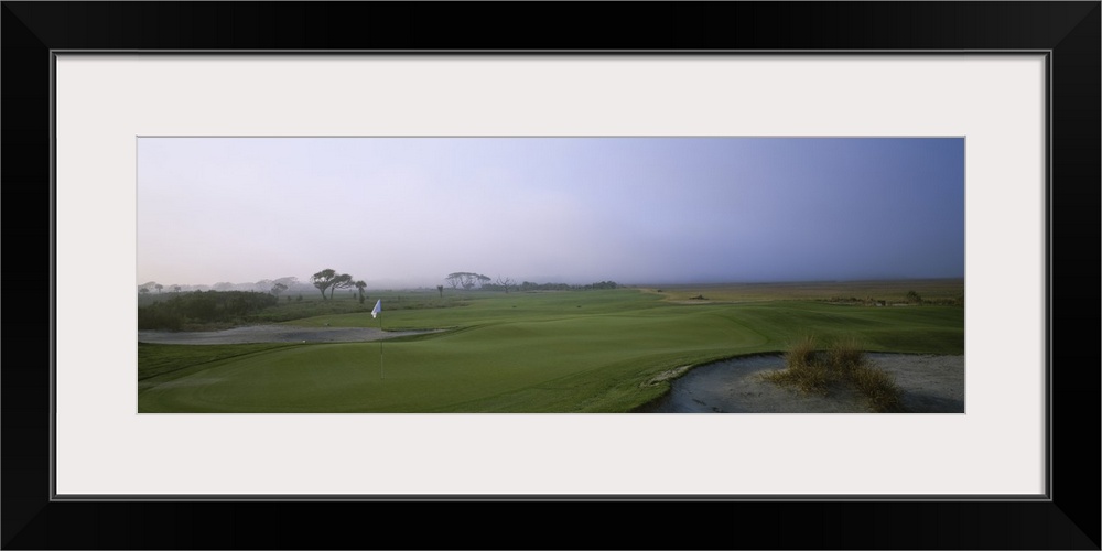 Giant landscape photograph of a flag surrounded by the rolling greens on Ocean Golf Course, beneath a hazy blue sky on Kia...