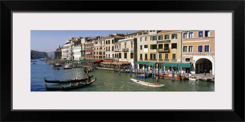 Large panoramic of a busy canal in Venice, Italy with gondola's and boats floating on the water and tourists walking along...