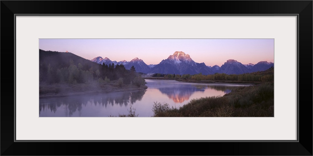Wide angle photograph taken from across a body of water looking out at a mountain range during sunrise.
