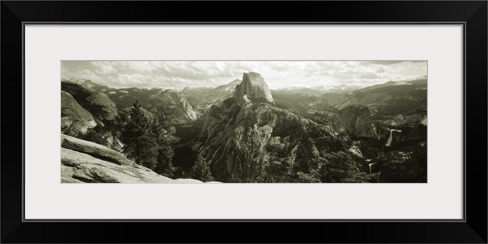 Panoramic photograph of mountain range under a cloudy sky with cliff's edge in foreground.