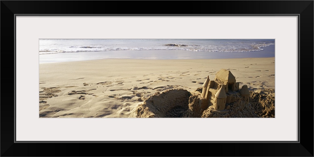 This landscape photograph of a sandy beach has a elaborate well build castle in the foreground surrounded by a tiny moat t...