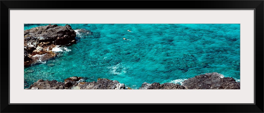 This panoramic photograph shows two figures from distance in clear waters of a reef.