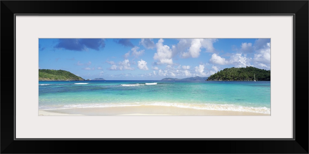 Panoramic photo of a white sand beach with crystal clear water and two land masses off in the distance on either side.