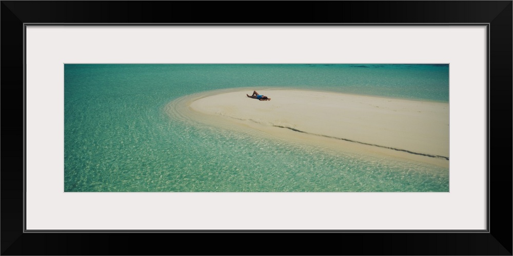 Panoramic photograph of girl tanning on sand bar surrounded by crystal clear ocean.