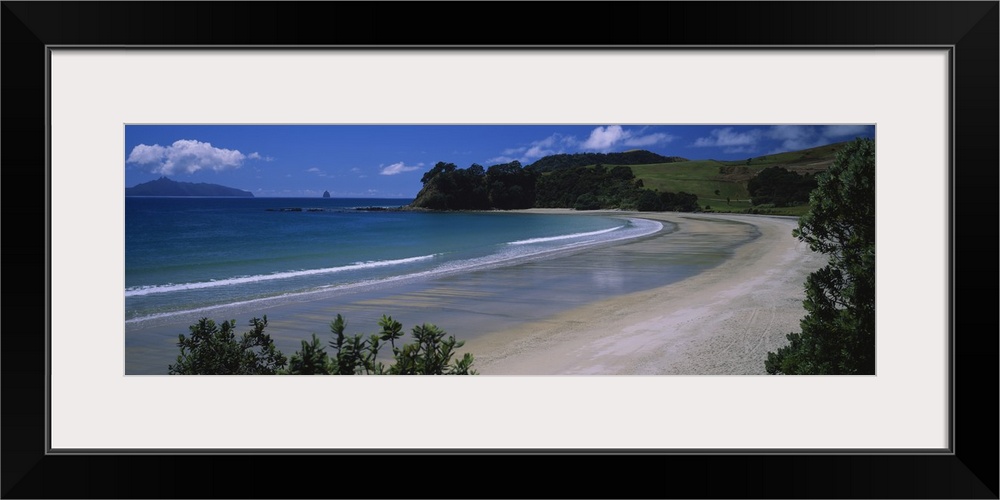 This large panoramic photograph is taken from the New Zealand coast with a large hill in the distance and water breaking o...