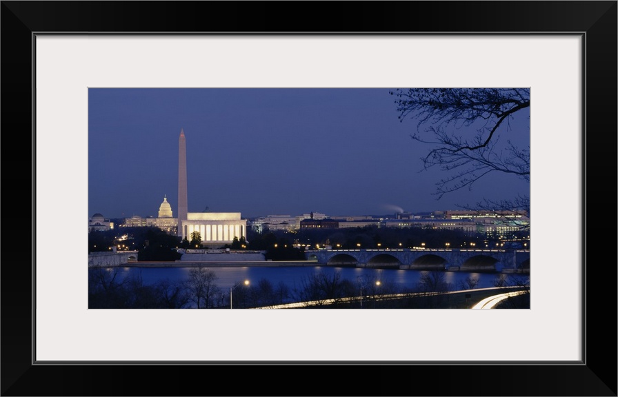 Wall art of major illuminated DC landmarks layered in the distance of a waterfront that a bridge passes over at dusk.