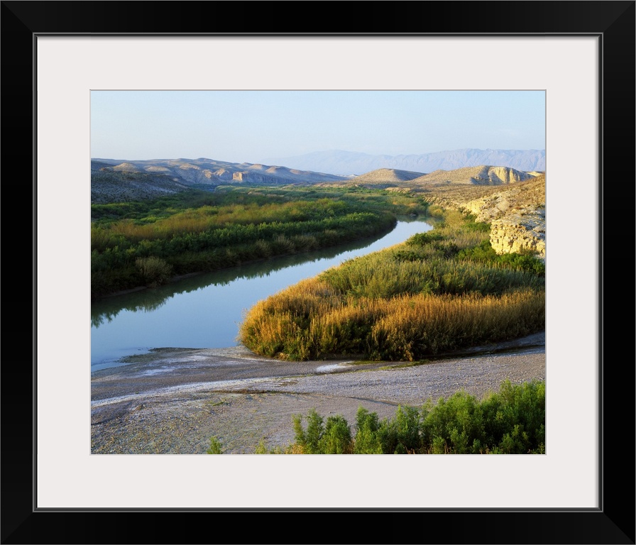 This photograph was taken inside Big Bend national park showing the river that has large brush lining it on either side. H...