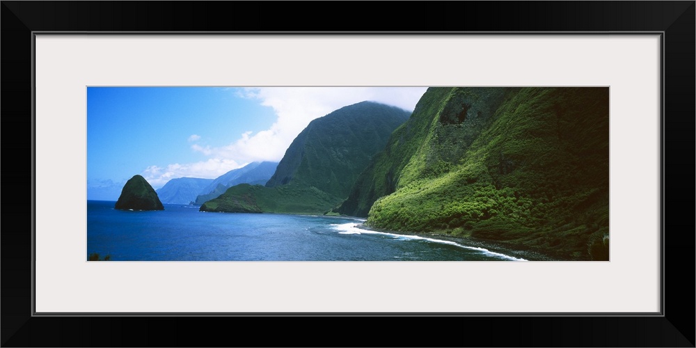 Panoramic photo of large tropical mountains meeting the ocean with a small mountain off shore.