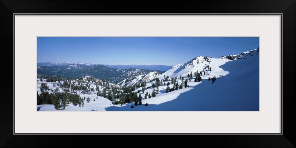 A panoramic photograph looking down a snow covered mountain into the valley below.