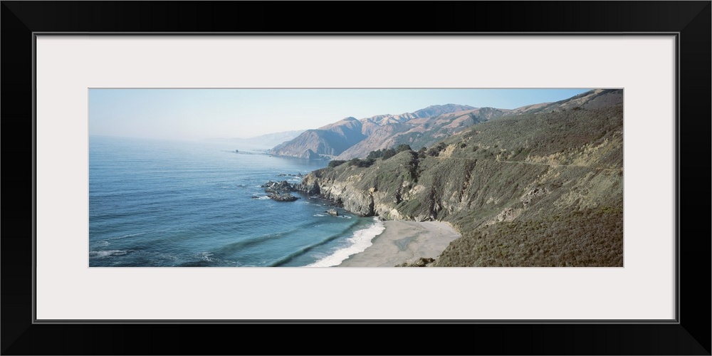 Panoramic image of the Pacific Ocean meeting rocky cliffs and a smooth beach.