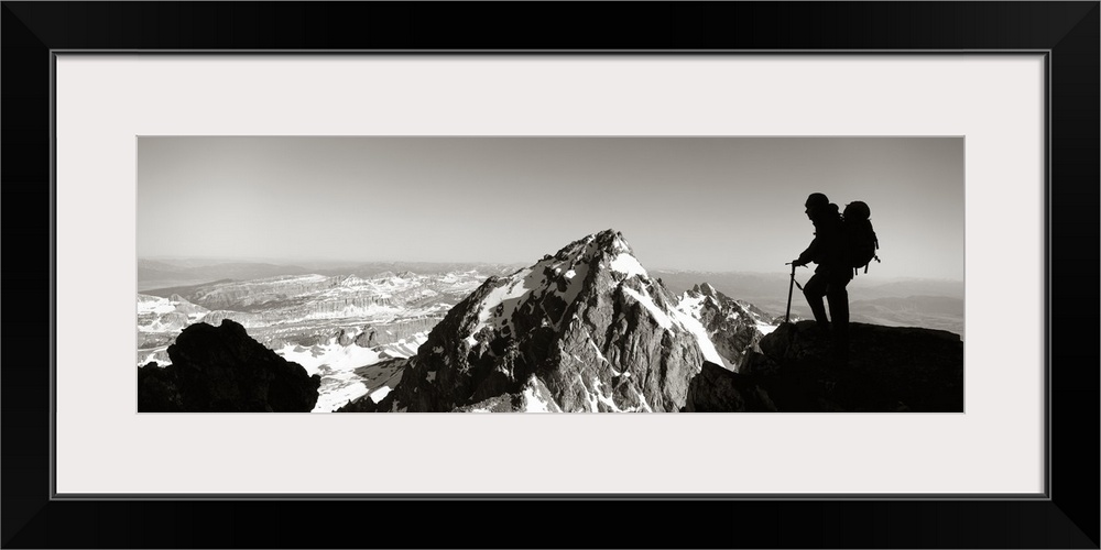 This panoramic photograph shows mountain peaks and the silhouette of a climber surveying the landscape.