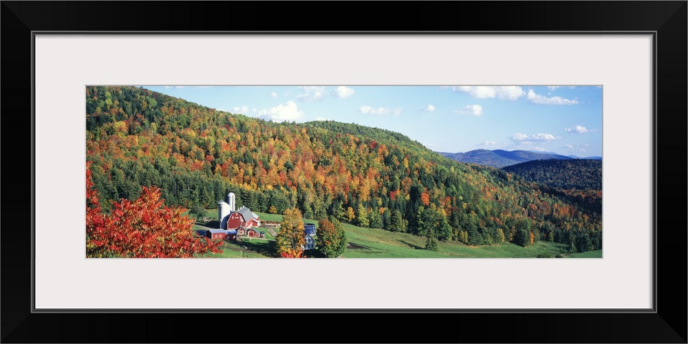 This decorative wall accent for the home or workspace is a panoramic photograph of a farm in the hills surrounded by trees...