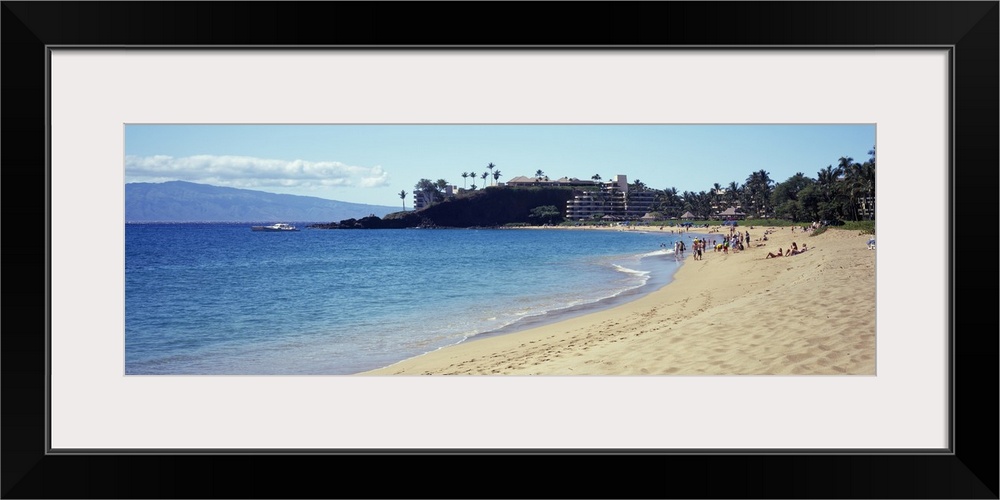 Wide angle photograph taken of a Hawaiian coast with people on the beach and a hotel in the distance.