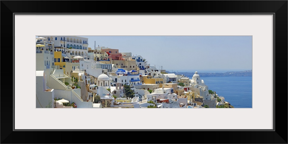 Houses in Greece are photographed from the side as they sit high up in a large cliff off the coast.