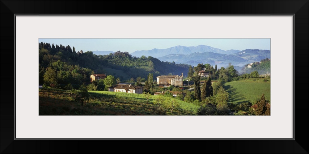 Giant, landscape photograph of rolling green hills and tress surrounding several houses in Marches, Italy.  A large mounta...