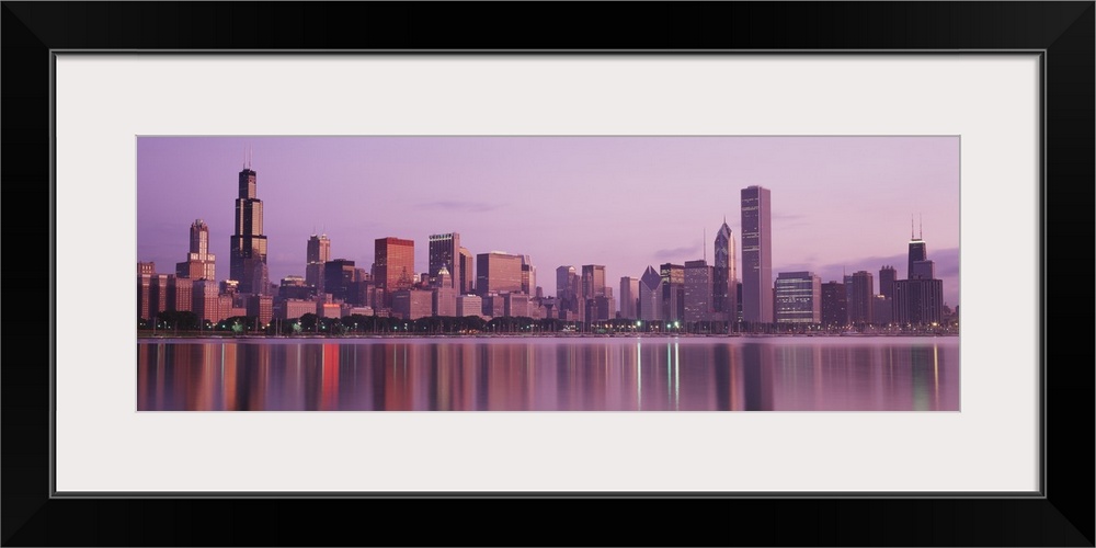 Panoramic photograph of skyline and waterfront lit up at dusk.  The buildings are reflected in the water below.