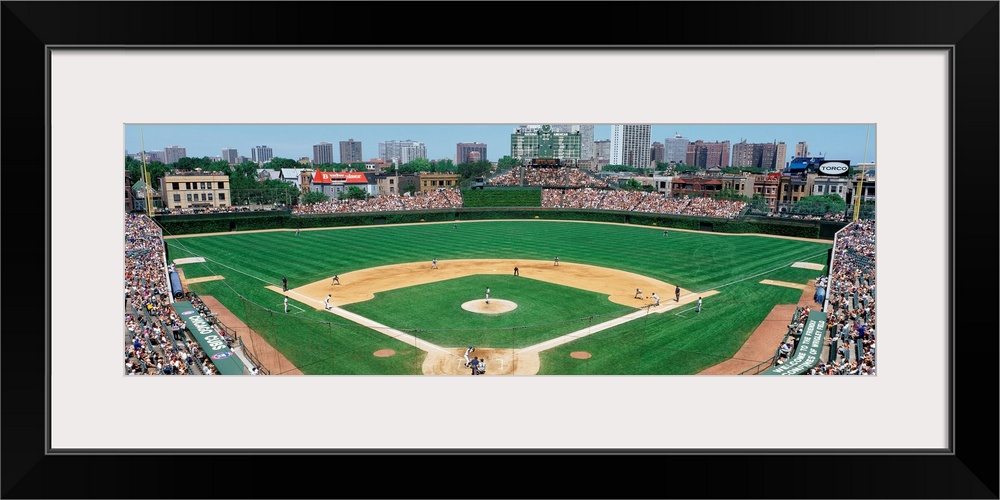 Panoramic photograph of Wrigley Field with Chicago skyline in the distance.  Stadium is full of people and the players are...