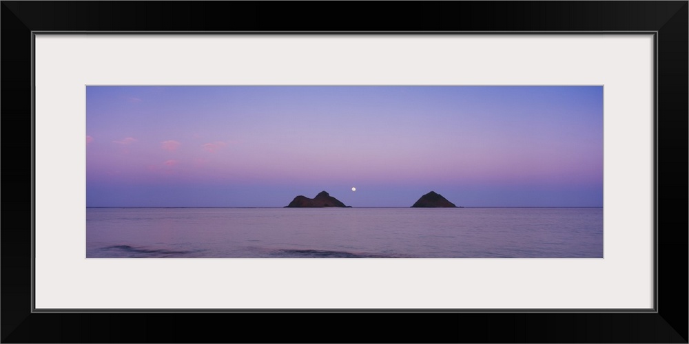 Giant horizontal photograph of a pastel sky over the water near Oahu, Hawaii, the Na Mokulua Islands on the horizon, at dusk.