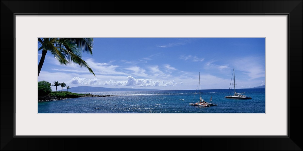 Panoramic photograph taken of a bay in Hawaii with land and palm trees on the left side and two boats anchored in the water.