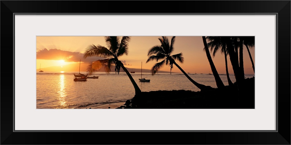 Panoramic photograph of a colorful sunset in the town of Lahaina on the island of Maui in Hawaii.  The bright sun shines o...
