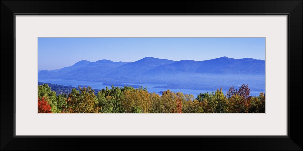 Panoramic photograph on a large wall hanging of the tops of autumn trees in front of Lake George, the Adirondack Mountains...