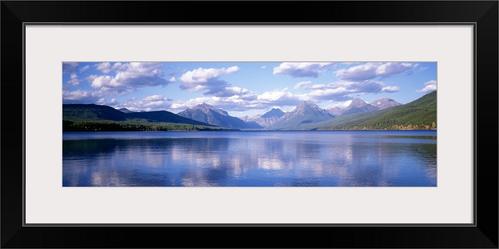 Panoramic photograph Lake McDonald with small ripples in the water reflecting the mountains and trees in the background.